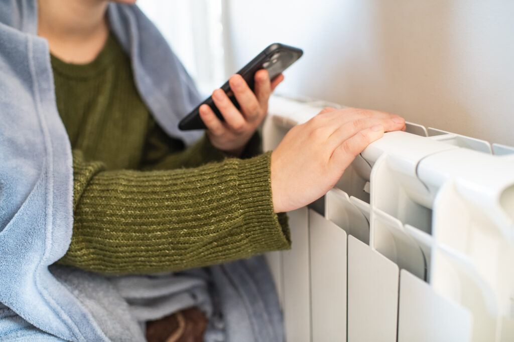 Young woman trying to warm near a radiator in winter, close-up