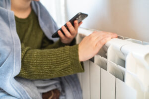 Young woman trying to warm near a radiator in winter, close-up
